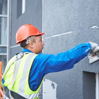 Facade worker covering external wall of building with plaster